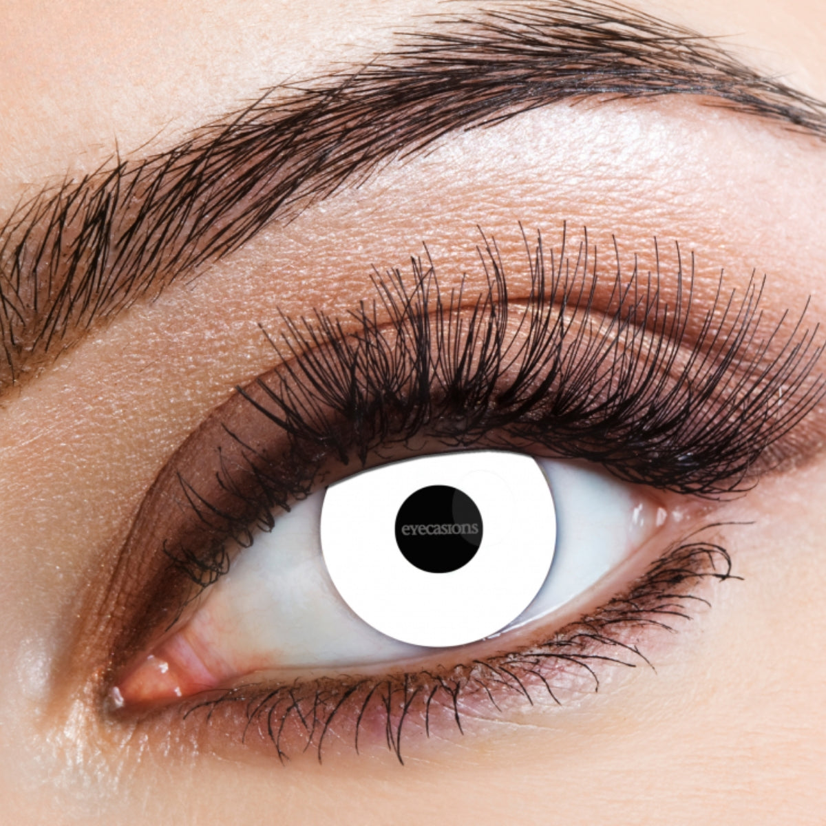Extreme close-up of a human eye wearing a white contact lens with a black pupil center and the brand name 'eyecamo' visible, with brown eyeshadow and mascara on the surrounding eye area.
