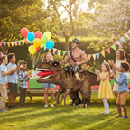 Man in inflatable T-Rex shoulders costume at garden birthday party with children - lifestyle image