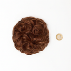 Flat lay of warm auburn copper curly messy hair bun 33/30 Sunrose beside a £1 coin showing product size, clean white background with soft overhead lighting