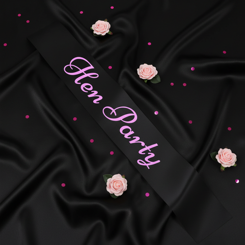 Black hen party sash with pink writing displayed on black satin with pink roses and confetti