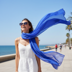 Woman laughing at the seaside with a blue chiffon scarf billowing in the ocean breeze