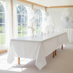 White plastic tablecloth on a long banquet table in a bright party hall with natural window light