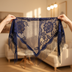 Close-up of hands holding a navy blue lace triangle shawl showing intricate floral embroidery pattern and long tassel fringe detail