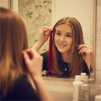 Young woman clipping in a vivid cherry red Stargazer hair extension in front of a mirror, candid self-expression moment