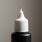 Extreme macro close-up of Technic Essentials Nail Glue precision tip applicator nozzle showing clear adhesive bead and matte black bottle finish