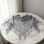 Grey vintage triangle shawl with floral lace cut-out pattern and fringe trim on elegant neutral background