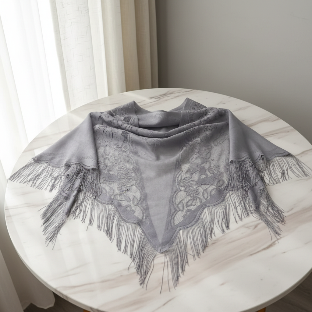 Grey vintage triangle shawl with floral lace cut-out pattern and fringe trim on elegant neutral background