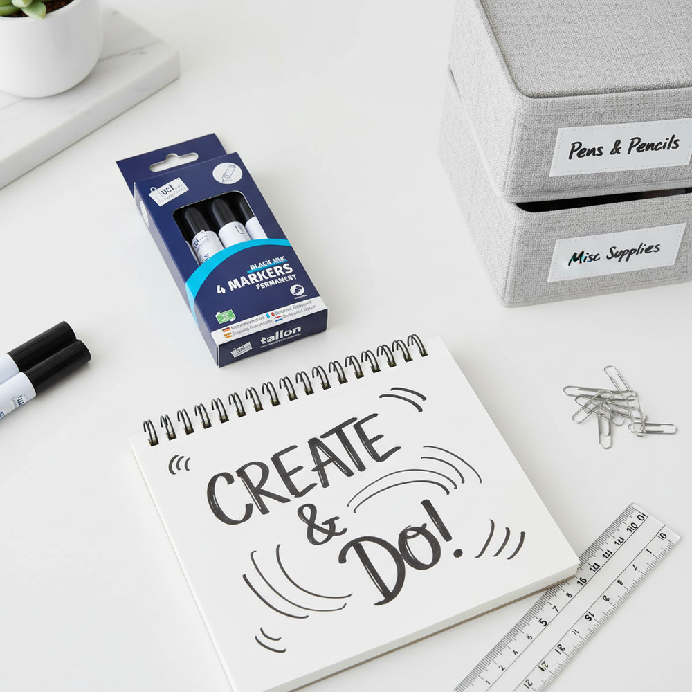 Flat lay of Tallon 4 pack black permanent markers with sketchbook and stationery on a white desk