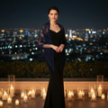 Elegant woman wearing a navy blue lace fringe triangle shawl over an evening dress on a candlelit luxury hotel terrace at night