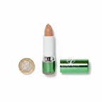 W7 Tea Tree Concealer Stick Medium/Deep flat lay beside £1 coin for size reference, white background with soft overhead lighting showing metallic green casing