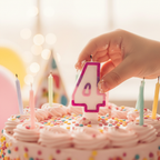 Child placing pink glitter number 4 birthday candle onto a birthday cake, candid moment with warm bokeh background