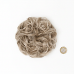 Flat lay of cool ash blonde curly messy hair bun 112 Ash Moon beside a £1 coin showing product size, clean white background with soft overhead lighting