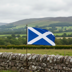 Scotland flag hanging on a traditional Scottish stone cottage wall with green countryside landscape in the background