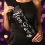 Close-up of black satin hen party sash with sparkling diamante embellishments held in hands against party bokeh