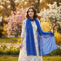 Stylish woman wearing a lightweight blue chiffon scarf walking through a spring park at golden hour