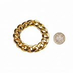 Chunky gold bracelet beside a £1 coin on white background showing product size — flat lay
