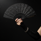Elegant hand holding open black lace fan in glamorous masquerade setting
