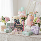 Pink floral birthday gift bag styled on a party table with presents and birthday cake