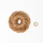 Flicky honey blonde wavy scrunchie hairpiece flat lay beside British £1 coin to show scale — white background overhead lighting