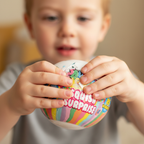 Candid shot of child opening HTI Squish Surprise Ball with curiosity, 85mm bokeh background, warm colour grade