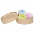 3 kawaii squishy bao bun dumplings in blue, yellow-green and pink with kawaii faces, displayed in an open bamboo steamer basket on a pure white background