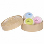 3 kawaii squishy bao bun dumplings in blue, yellow-green and pink with kawaii faces, displayed in an open bamboo steamer basket on a pure white background