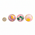 Three sensory putty balls in assorted designs on white background beside a £1 coin to show size scale
