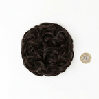 Flat lay of dark brown curly messy hair bun 2 Nigella beside a £1 coin showing product size, clean white background with soft overhead lighting