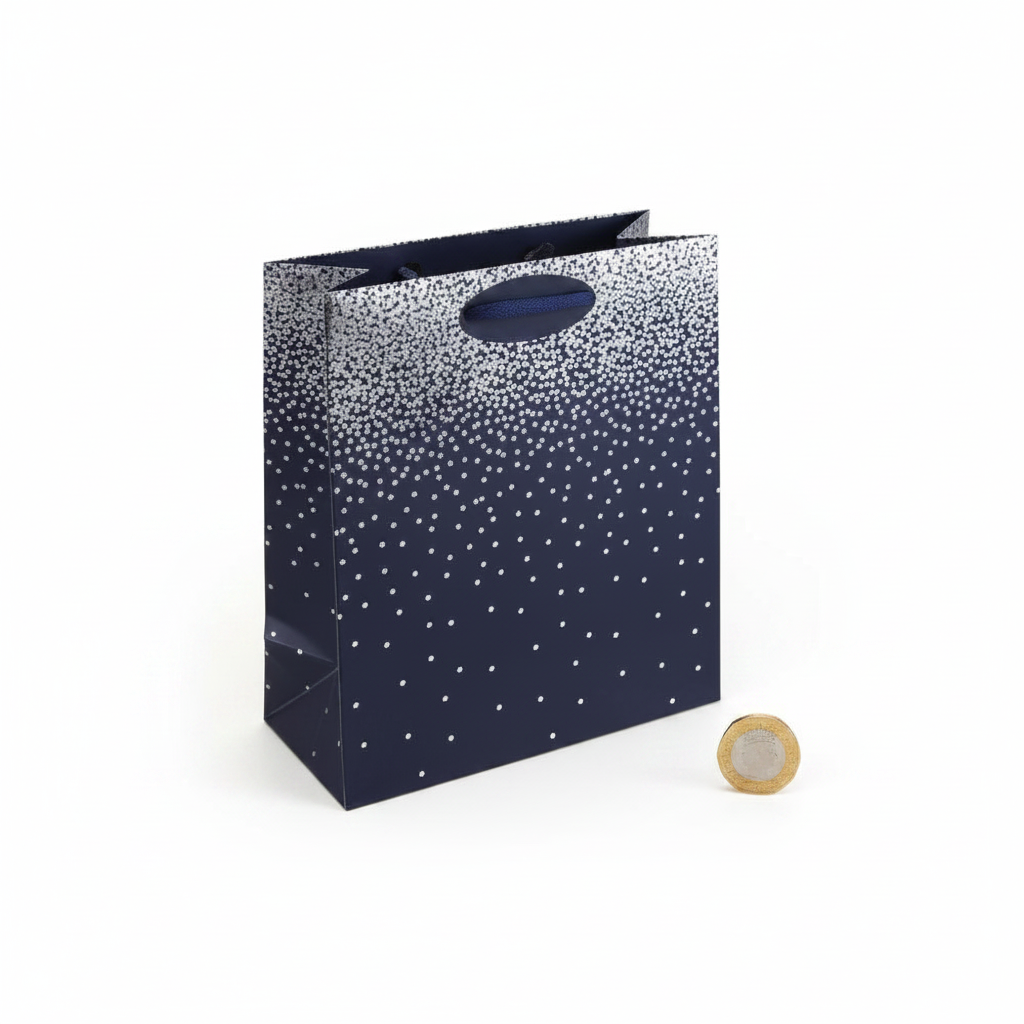 Navy ombre medium gift bag with silver dot pattern placed beside a £1 coin on white background to show size