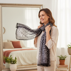 Woman styling a black and grey chiffon leopard print scarf in front of a bright bedroom mirror