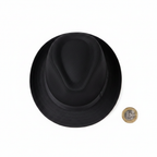 Adults black trilby hat flat lay on white background beside a £1 coin to show scale and size