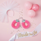 Flat lay of pink fur handcuffs with hen party props on pastel pink background