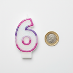 Pink glitter number 6 birthday candle flat lay beside a £1 coin showing product scale, white background overhead lighting