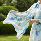 Close-up of hands holding a flowing light blue chiffon scarf showing bold blue floral print and green leaf detail in natural daylight
