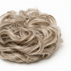 Extreme macro close-up of cool ash blonde curly hair bun 112 Ash Moon showing individual curl texture, pale ash silver sandy tones and strand craftsmanship