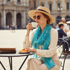 Stylish woman at a European outdoor café wearing a teal turquoise floral chiffon scarf with mushroom ruffle edges, sipping coffee