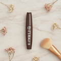 W7 It's Really Colour Mascara in Brown standing upright on a warm marble surface with dried flowers and a makeup brush, premium beauty product shot