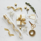 Flat lay of gift wrapping supplies including clear cellophane roll, scissors, ribbon and gift tags on marble