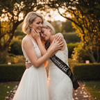 Bride and bridesmaid sharing emotional moment in garden wedding setting bridesmaid wearing sparkling black satin diamante sash at golden hour