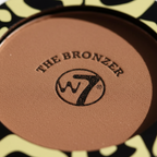 Extreme macro close-up of W7 The Bronzer Matte Bronzing Powder Compact showing ultra-fine deep warm brown powder texture and embossed W7 logo detail