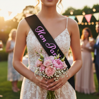 Close-up of black hen party sash with pink writing worn at an outdoor garden celebration at golden hour
