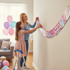 Mother and daughter hanging unicorn rainbow holographic birthday banner for party setup