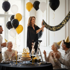Woman hanging 9ft black and gold 80th birthday banner at elegant party celebration