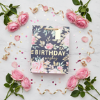 Flat lay of small pink floral birthday gift bag on marble surface with roses and confetti