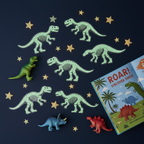 Flat lay of glow in the dark dinosaur sticker figures on dark navy background with glowing stars and dinosaur toys