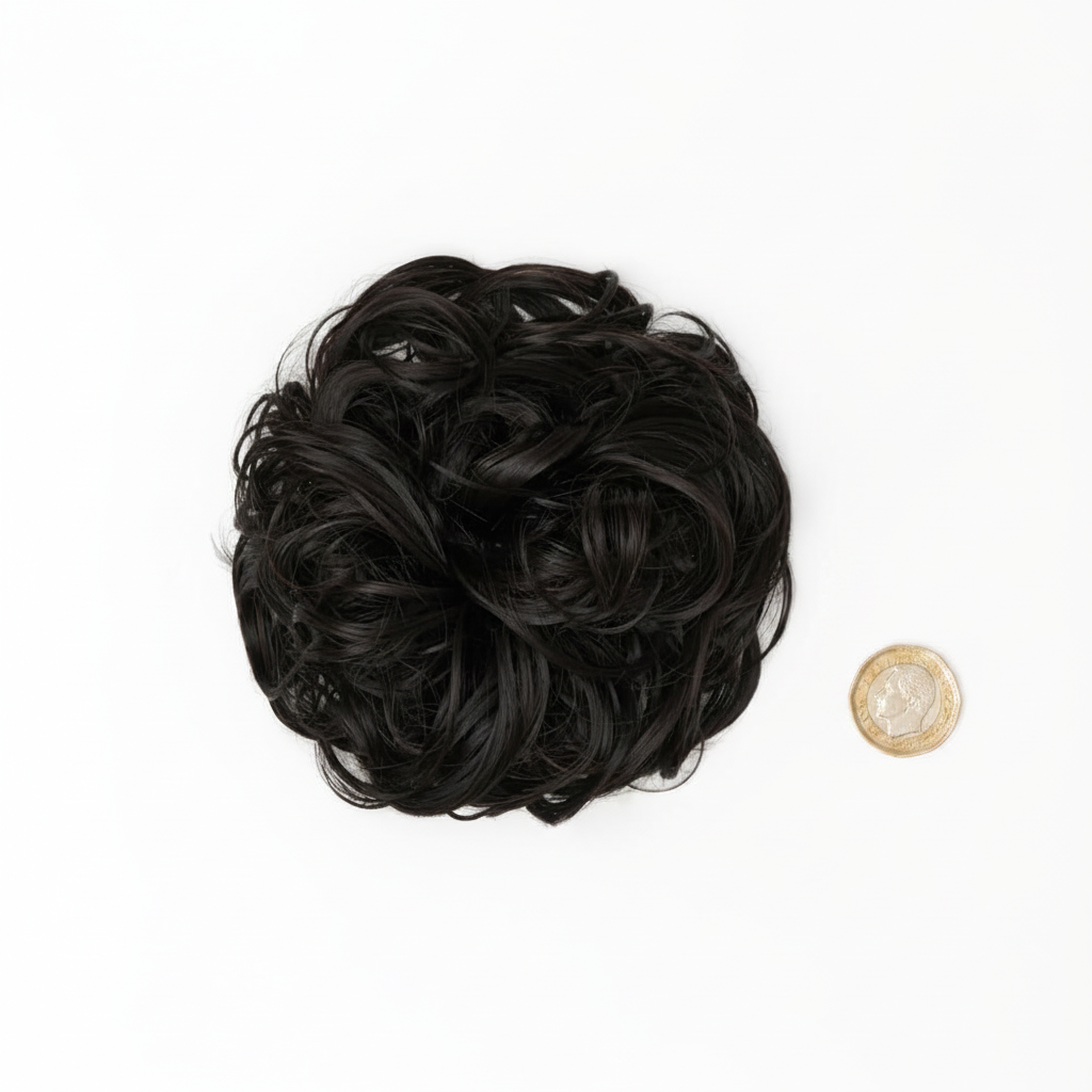 Flat lay of dark brown curly messy hair bun 1B Queen of the Night beside a £1 coin showing product size, clean white background with soft overhead lighting