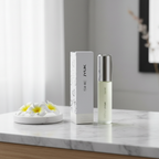 Milton Lloyd She JYUK perfume bottle and box on marble vanity with white flowers, natural window light