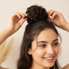 Woman styling her hair with a chocolate brown curly messy hair bun clip-in hairpiece shade 4 Chocolate Dahlia, candid natural moment with bokeh background