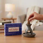 Hands placing a Satya Nag Champa warm brown backflow incense cone into a ceramic burner in a cosy home setting