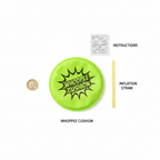Flat lay of whoopee cushion contents: neon green cushion, yellow inflation straw and instruction leaflet beside a £1 coin for scale
